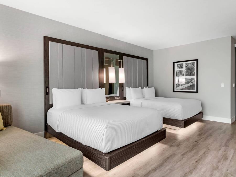 A hotel room with a large bed, a smaller bed, a sofa, a mirror, and a framed picture on the wall.