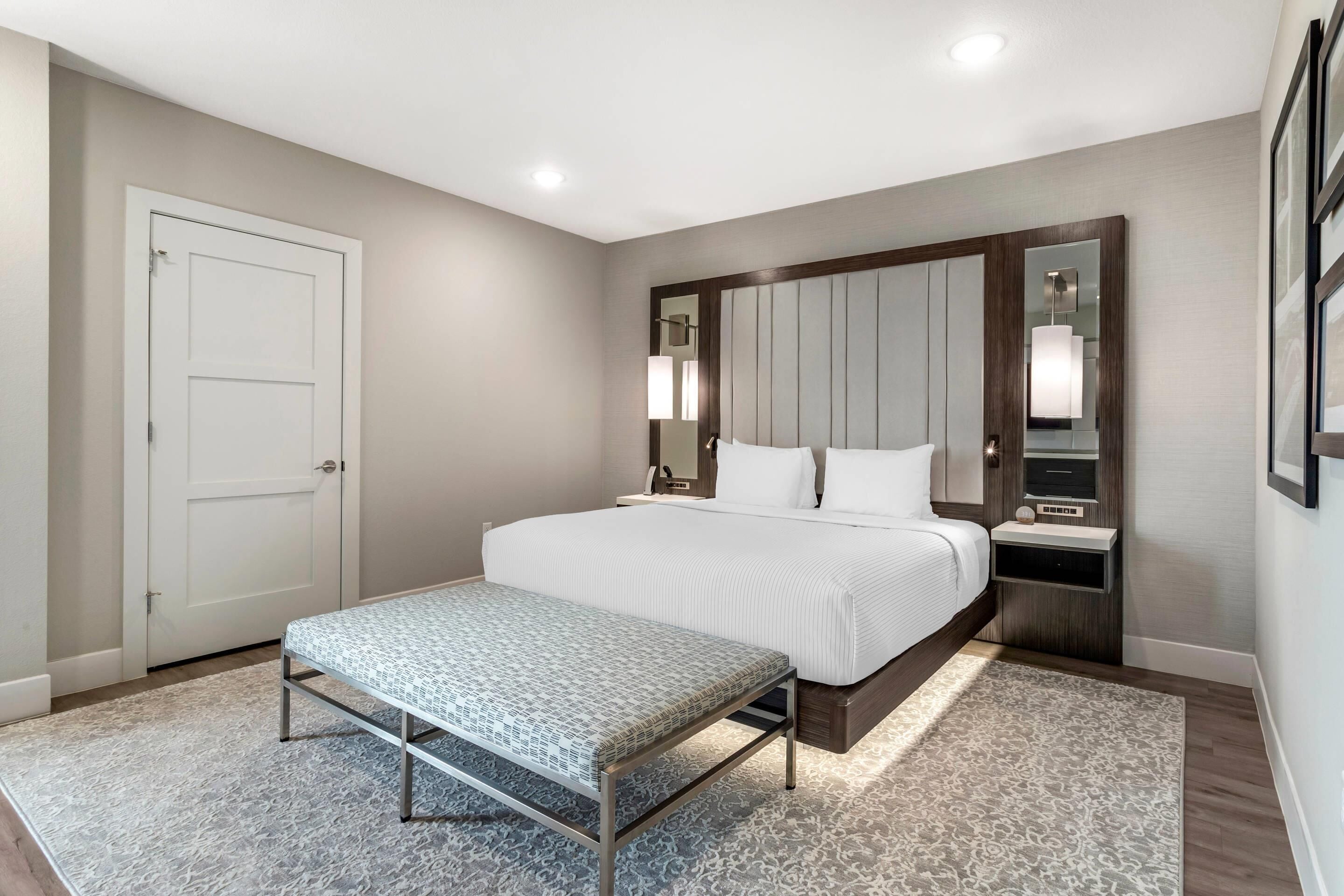 A modern bedroom with a large bed, bedside tables, a bench, and a mirror.