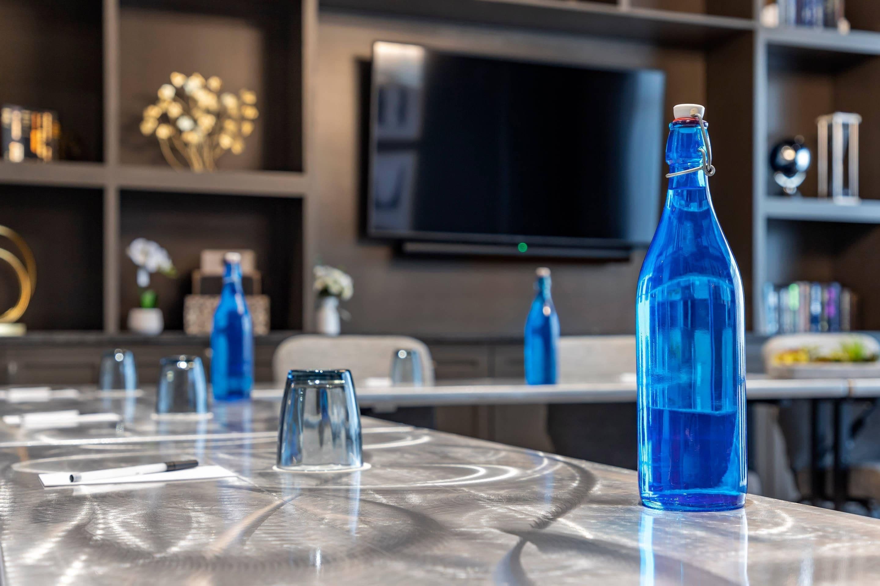 Un espace repas moderne avec une table en verre, des bouteilles en verre bleues et un téléviseur fixé au mur.