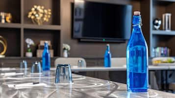 Un espace repas moderne avec une table en verre, des bouteilles en verre bleues et un téléviseur fixé au mur.