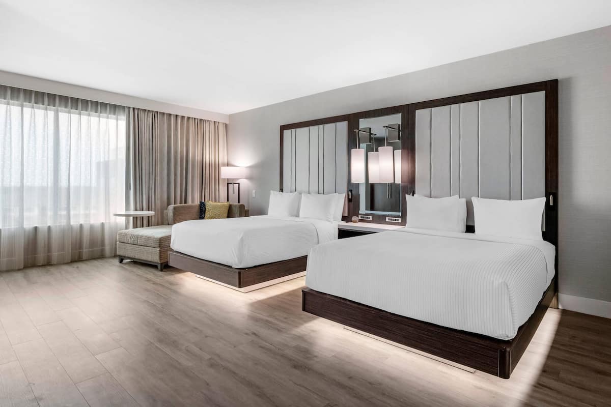 A hotel room with two beds, a bedside table, a lamp, and a large mirror.