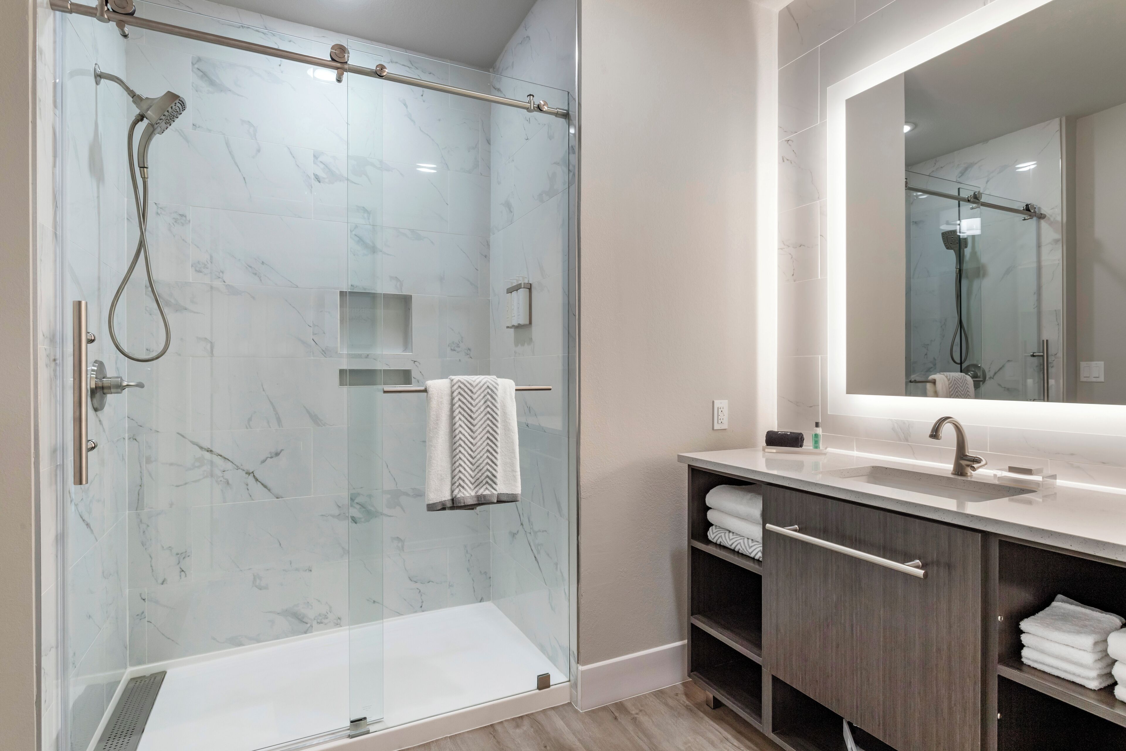 A modern bathroom with a glass-enclosed shower, a vanity with a mirror, and neatly folded towels.