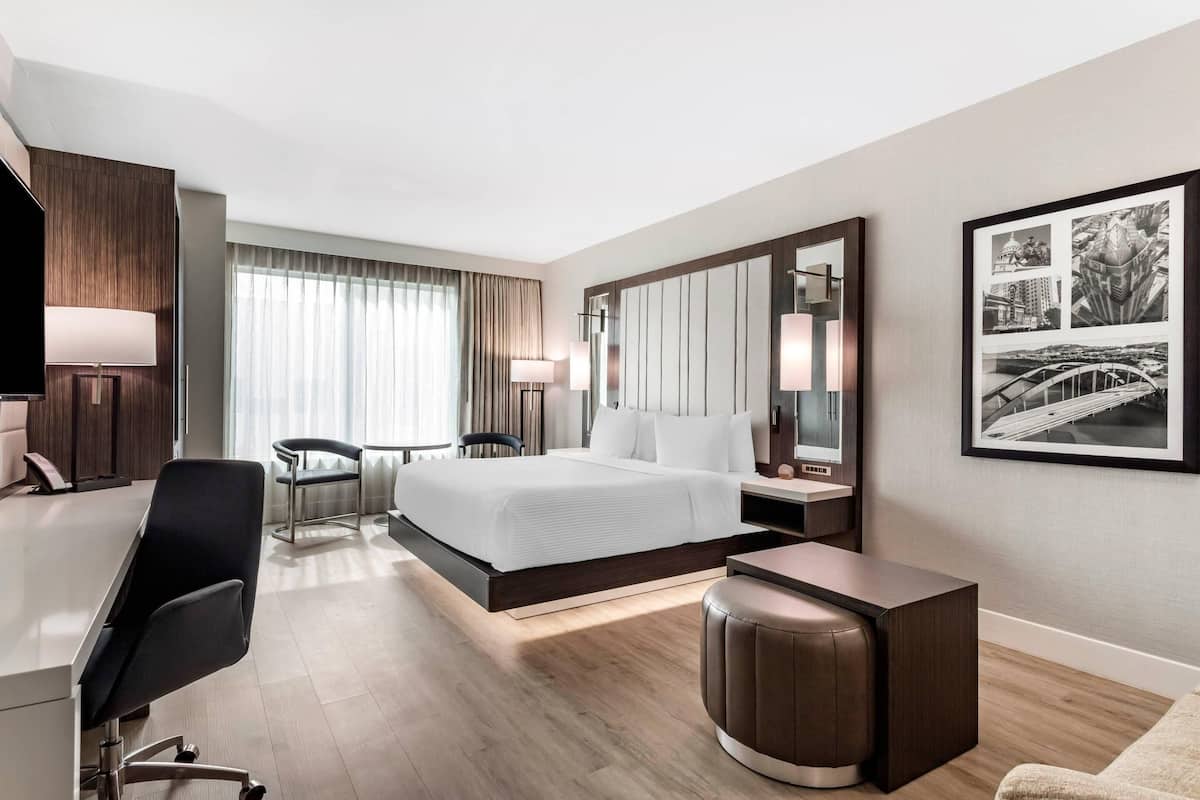 A modern hotel room with a large bed, a desk, a chair, a small table, and a large mirror.