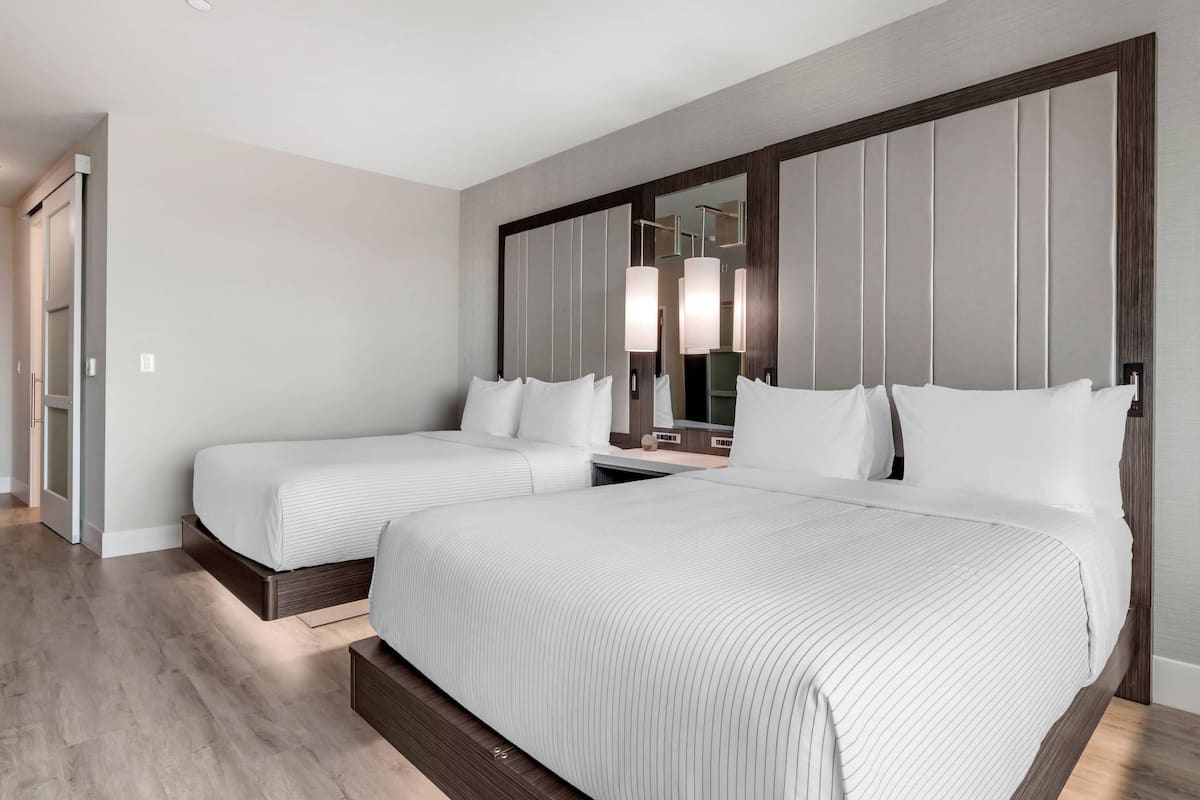 A hotel room with two beds, a large mirror, and a wooden floor.