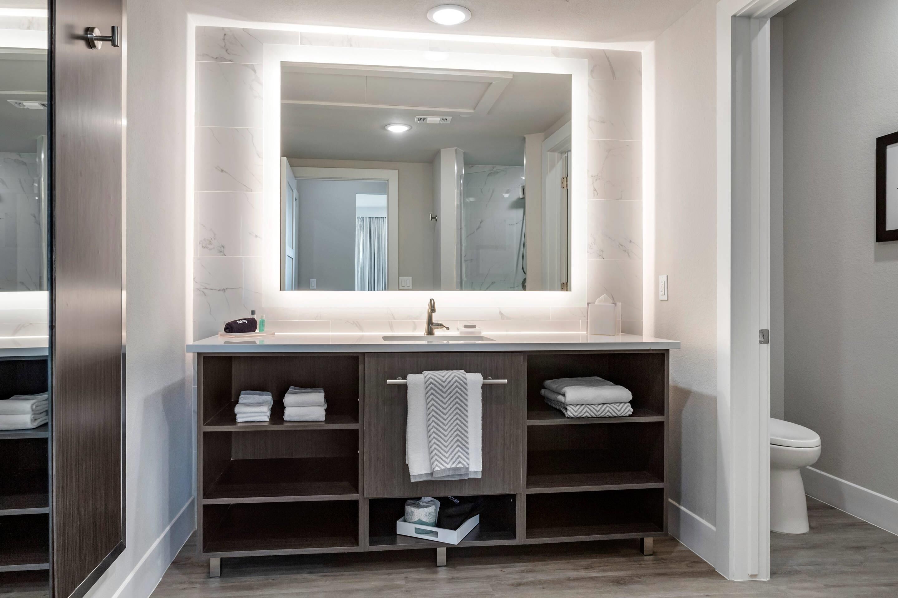 Un baño moderno con un espejo grande, estantes integrados, inodoro y zona de ducha.