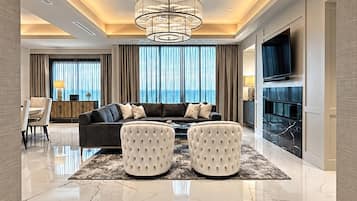 Una sala de estar moderna con un sofá, otomanas, un televisor y vistas al mar.