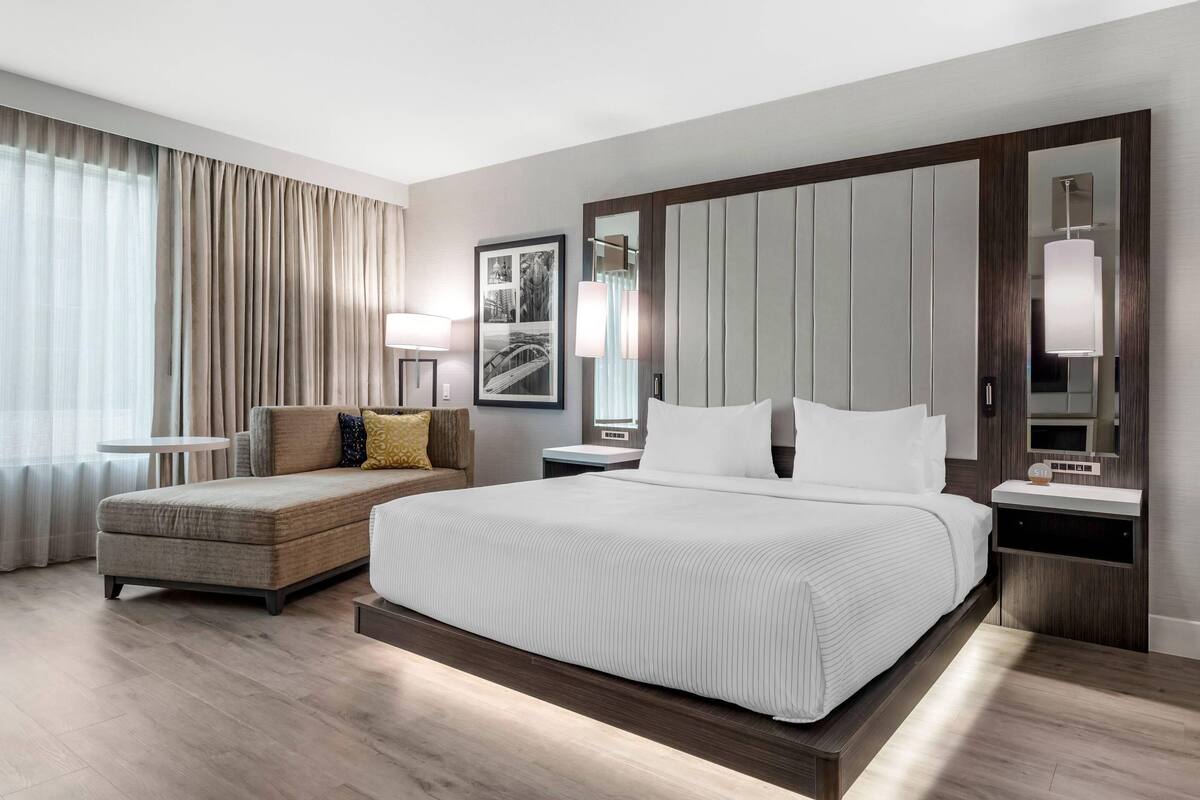 A modern hotel room with a large bed, a sofa, a small table, and a large mirror.