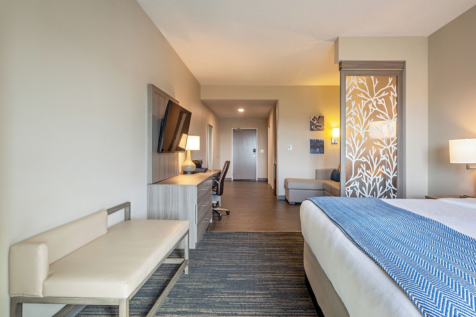 A hotel room with a bed, desk, chair, and a small sofa.