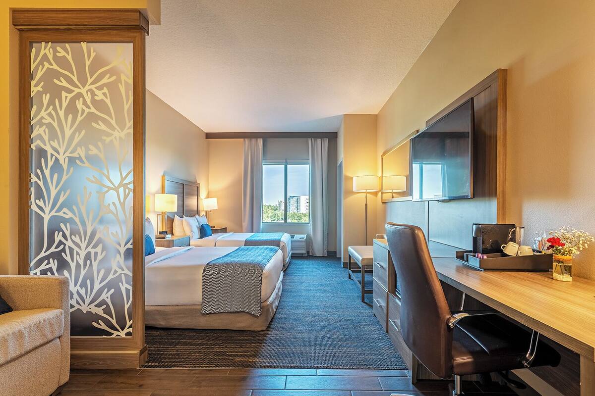 Une chambre d’hôtel avec deux lits, un bureau, une chaise, une télévision et une fenêtre avec des rideaux.