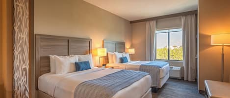A hotel room with two beds, a desk, a chair, and a window with curtains.