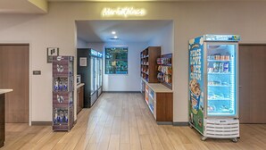 A corridor with a neon sign reading "Marketplace," vending machines, and shelves stocked with snacks and beverages.