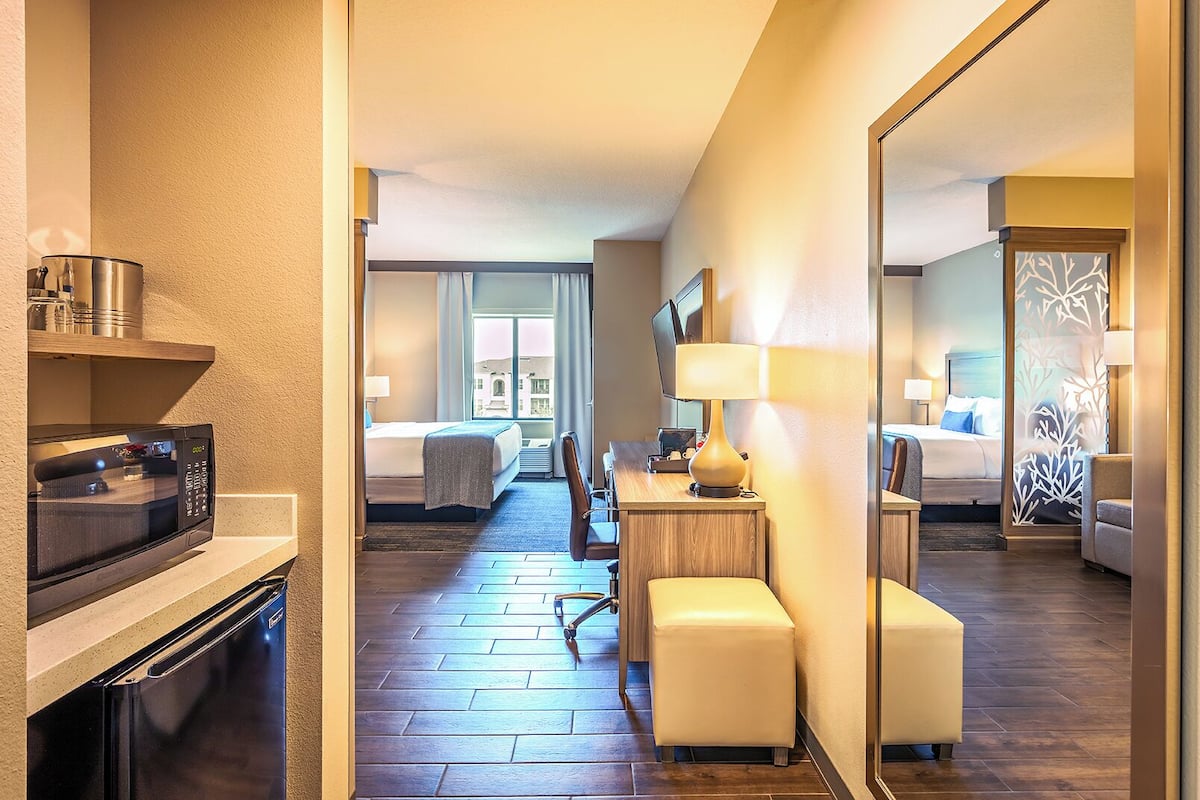 Une chambre d’hôtel comprenant un lit, un bureau avec une lampe, une chaise, un four à micro-ondes et un grand miroir.