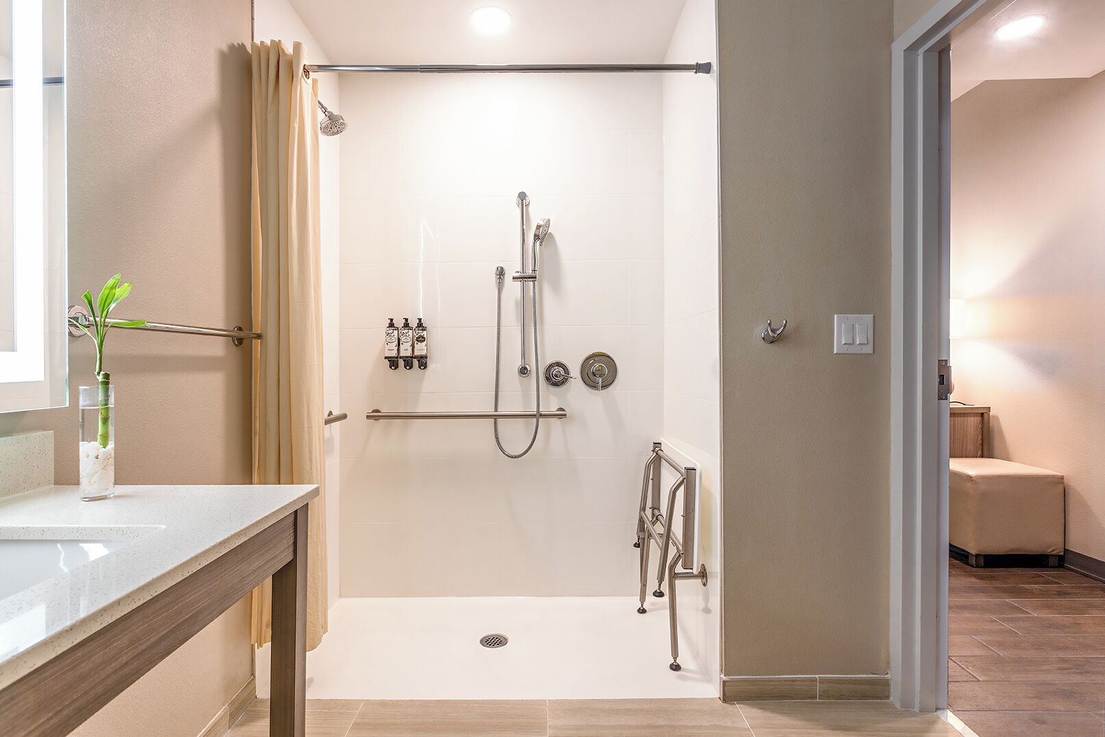 Un baño moderno con ducha a ras de suelo, un florero de vidrio con una planta y un perchero para toallas.