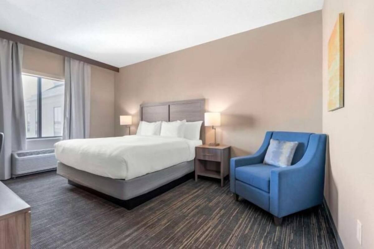 Une chambre d’hôtel avec un lit, une chaise, une table de chevet et une fenêtre.