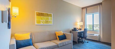 A hotel room with a sofa, a desk, and a window with curtains.