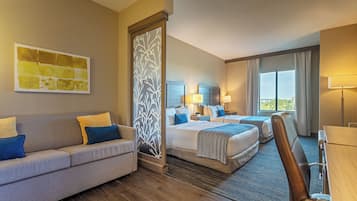 A hotel room with a sofa, two beds, a desk, and a large window.
