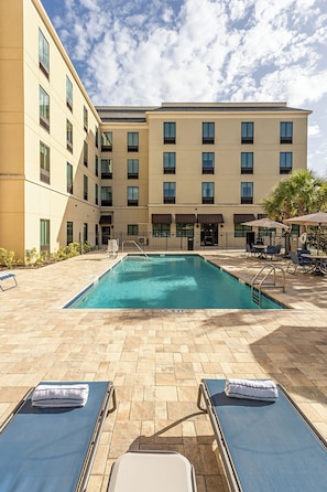 A hotel pool area with lounge chairs, a clear blue pool, and a building with multiple windows and balconies. - Pestana Orlando Suites - Lake Buena Vista (Orlando)