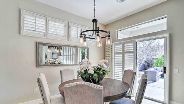 Un coin repas comprenant une table ronde, six chaises, un lustre, un grand miroir et une vue sur l’extérieur grâce à une porte-fenêtre coulissante.