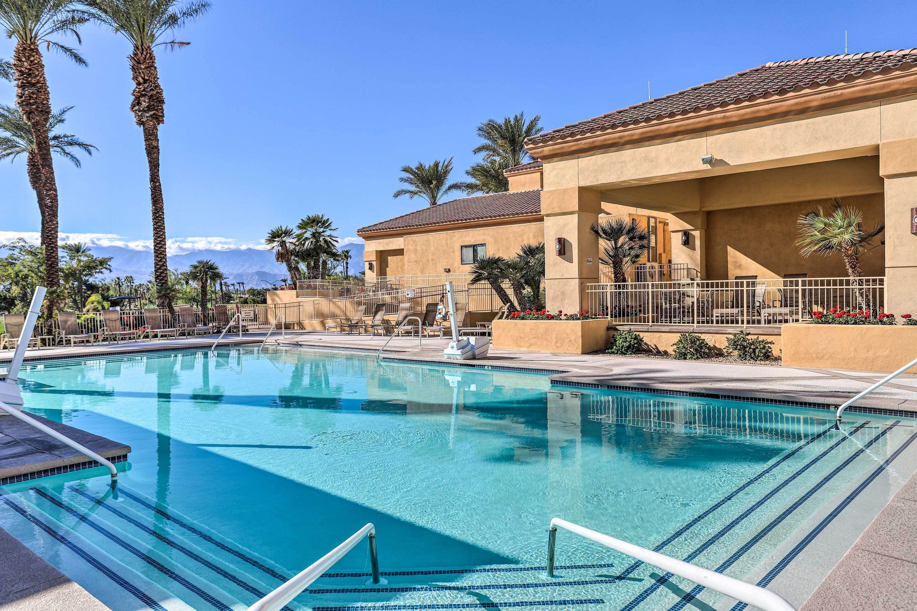 A swimming pool with clear blue water, surrounded by palm trees and a building with a tiled roof.
