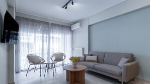 Un soggiorno moderno con un divano, due poltrone, un tavolino rotondo in legno e un televisore fissato alla parete.