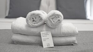 Un mucchio di asciugamani bianchi piegati con cura, accompagnato da un biglietto di ringraziamento, su una superficie grigia dalla trama interessante, probabilmente in una camera d'albergo.