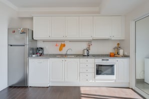 Una cocina moderna con armarios blancos, un refrigerador de acero inoxidable, un lavavajillas, un horno empotrado y una encimera de granito.