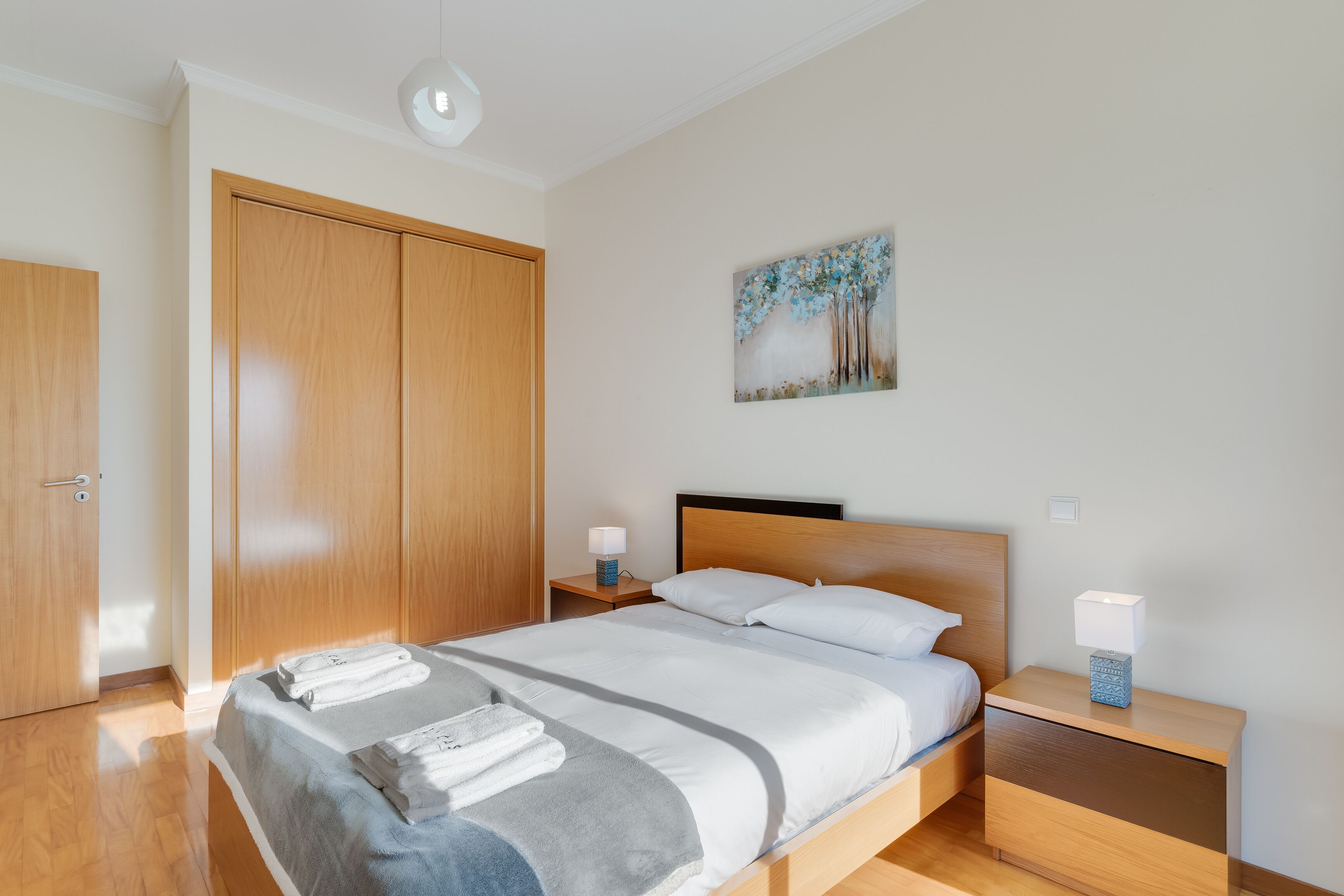 A modern bedroom with a large bed, wooden wardrobe, and a painting on the wall.