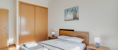 A modern bedroom with a large bed, wooden wardrobe, and a painting on the wall.