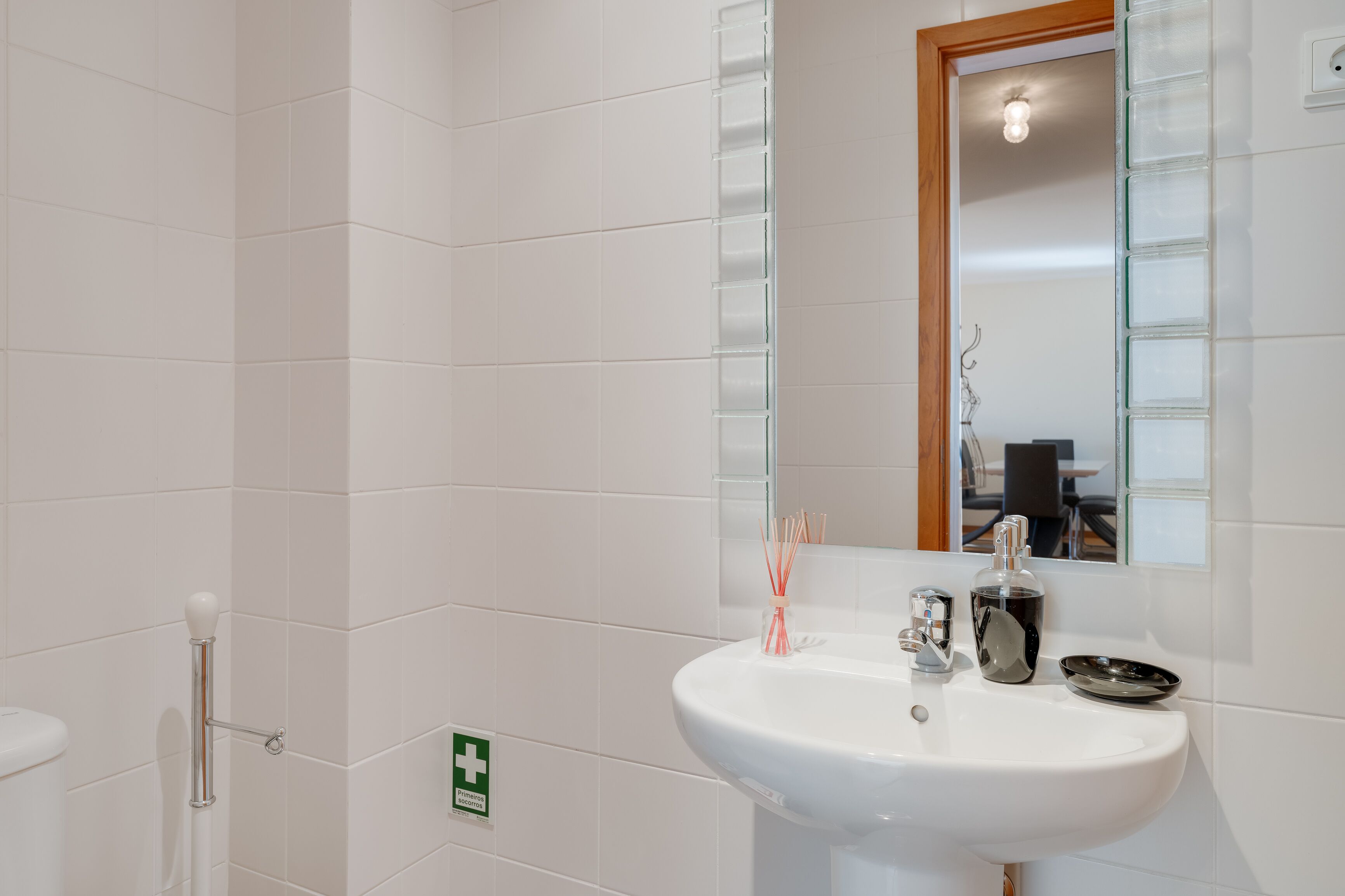 Ein Badezimmer mit weißen Fliesen, einem Waschbecken inklusive Spiegel und einer Duschkabine aus Glas.