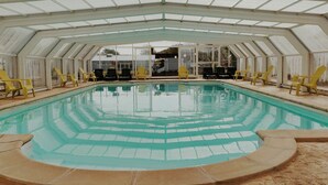 Ein Innenpool mit Glasdach, umgeben von gelben Stühlen.