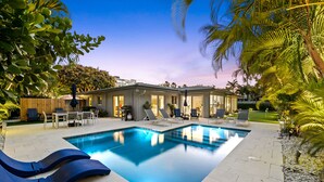 Ein Swimmingpool mit Liegestühlen, einem Grillplatz und einem Haus im Hintergrund.