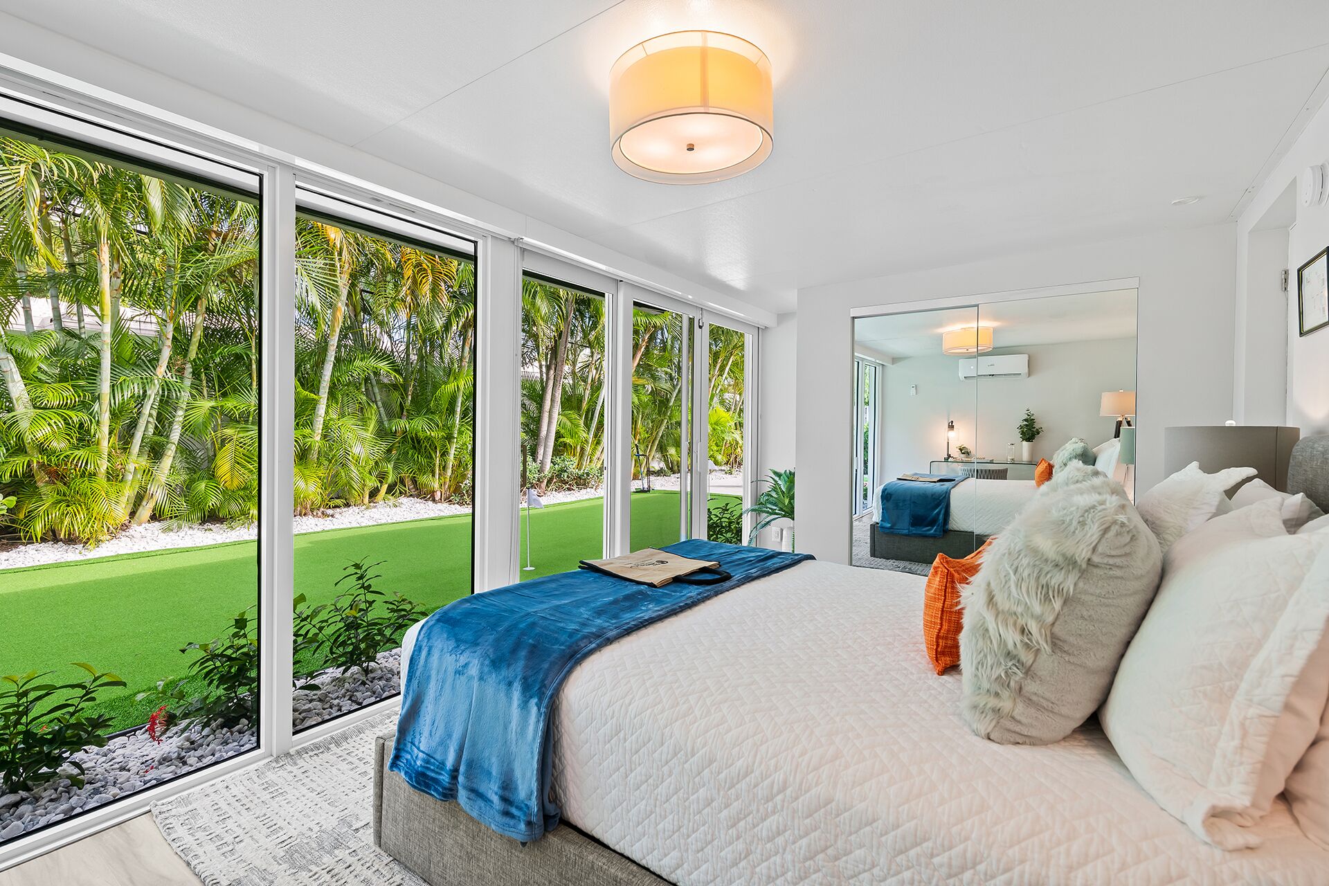A modern bedroom with a large bed, a view of a green lawn, and a sliding glass door leading to an outdoor area.