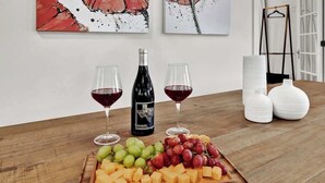 A wooden table with a cheese and fruit platter, two glasses of red wine, a wine bottle, and two white vases.