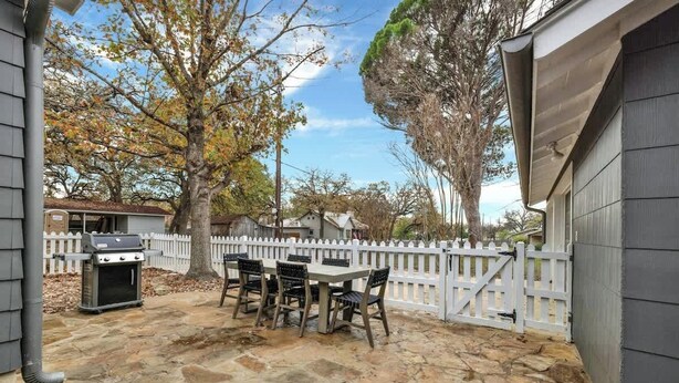 Une terrasse extérieure avec un sol en pierre, un barbecue et une table avec des chaises.