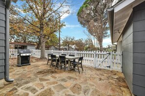 Un patio al aire libre con suelo de piedra, una parrilla y una mesa con sillas.