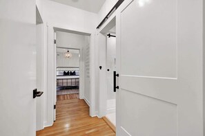 Un pasillo con paredes blancas y piso de madera que conduce a una cocina con mostrador e iluminación colgante.