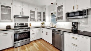 A modern kitchen with white cabinetry, stainless steel appliances, and a black countertop.