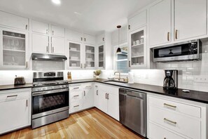 Una cocina moderna con muebles blancos, electrodomésticos de acero inoxidable y encimera negra.