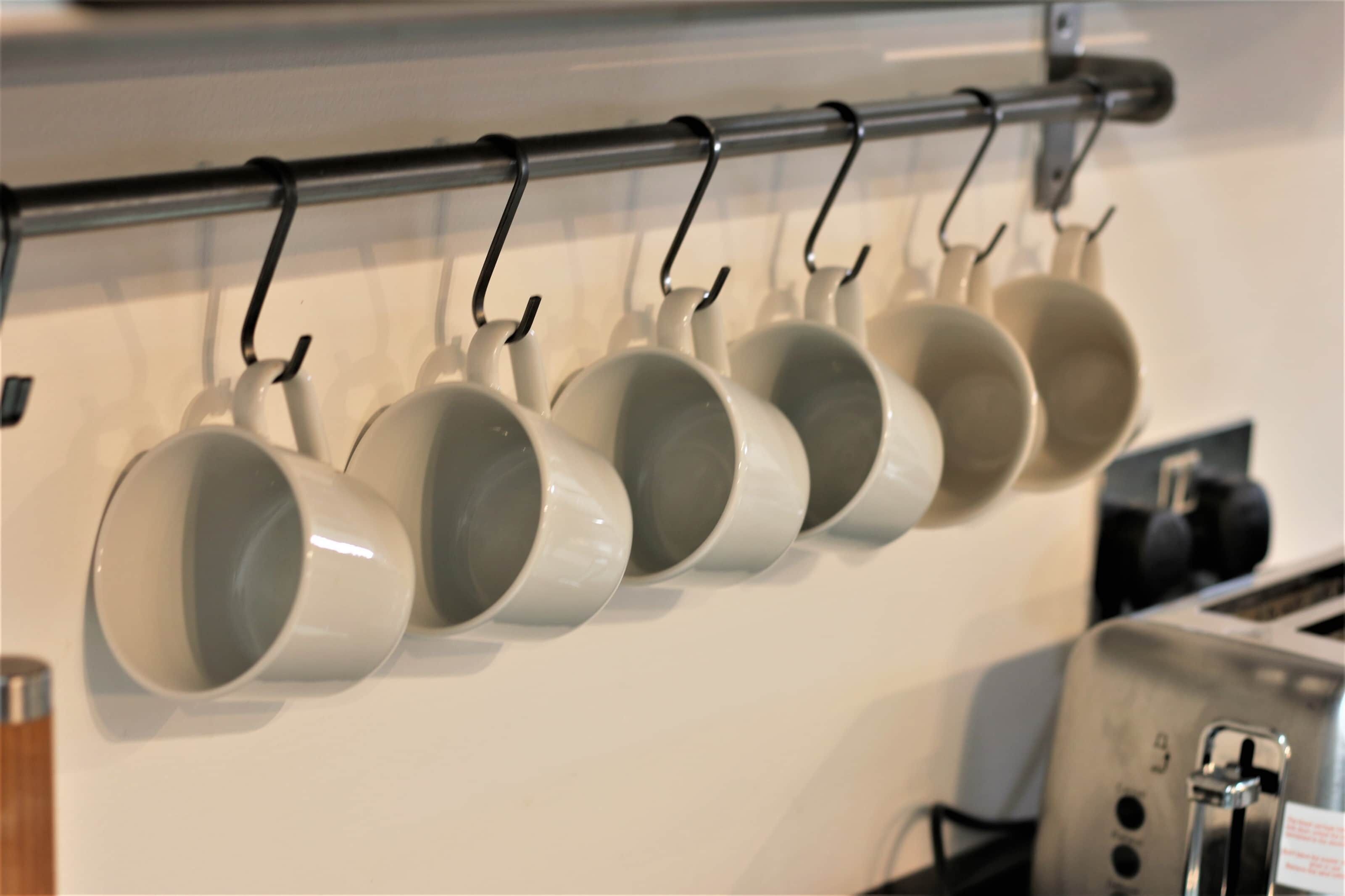 A kitchen with a row of white mugs hanging on a rack.