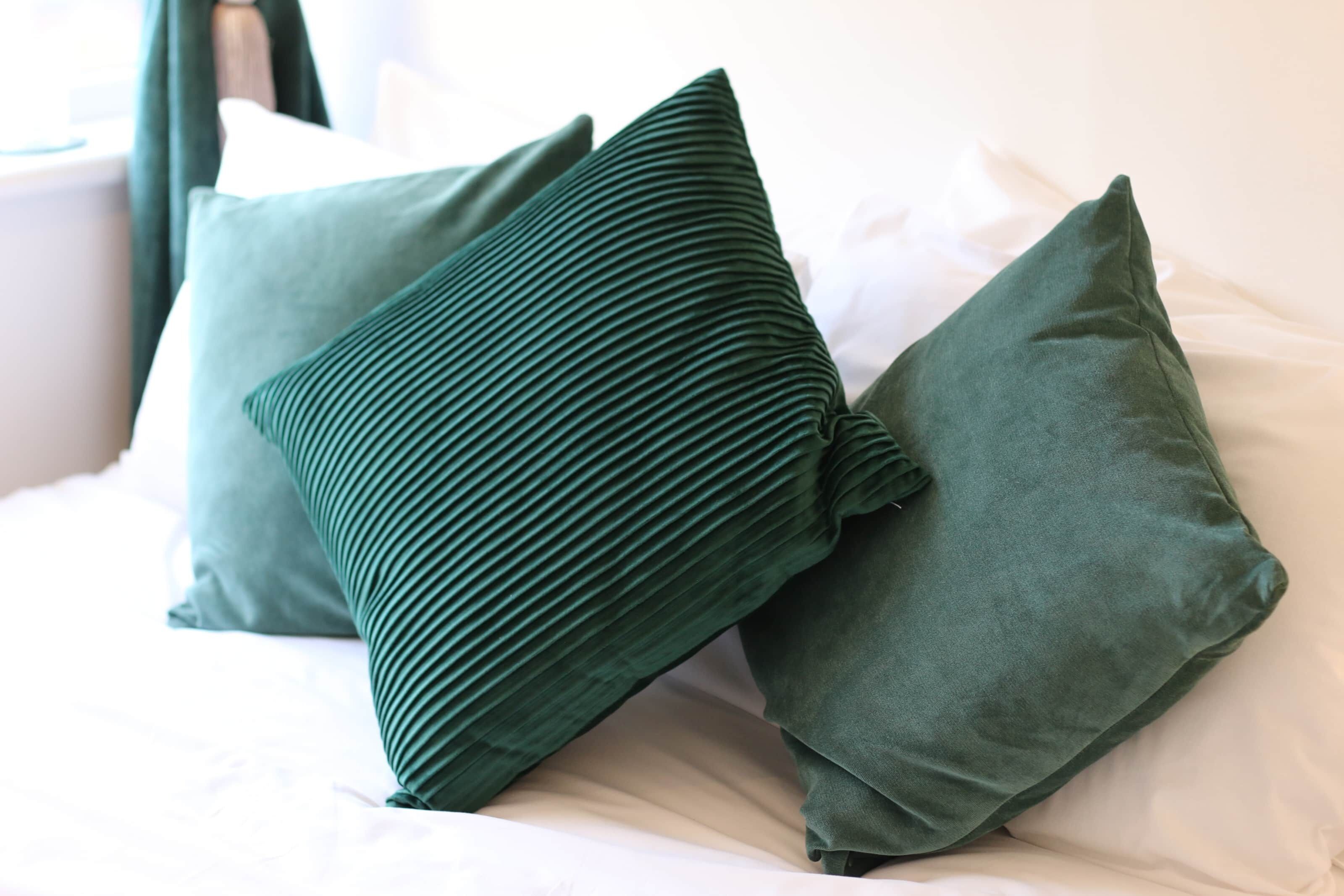 Una cama con dos almohadas verdes y una blanca.