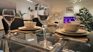 A dining table with clear glassware and white bowls, set in a modern room with a flat-screen TV and plants. - Ty Glas Mews (2 beds) (Cardiff)