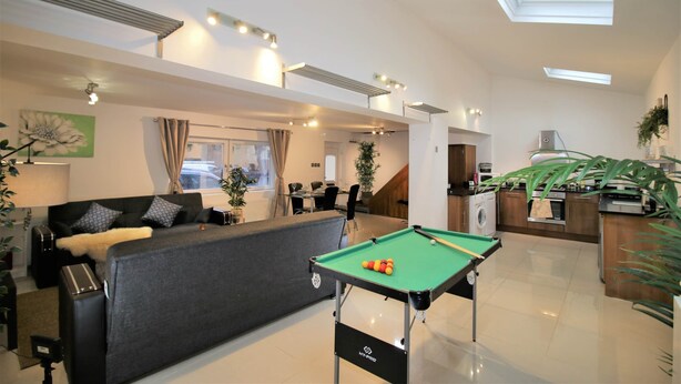 A modern living room with a pool table, sofa, and kitchen area. - Ty Glas Mews (2 beds) (Cardiff)