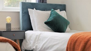 A neatly made bed with white linens and a teal headboard. - Thesiger 1 (3 beds) (Cardiff)