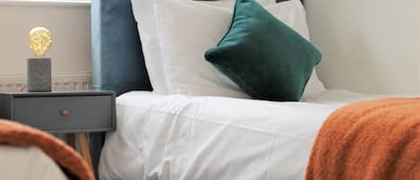 A neatly made bed with white linens and a teal headboard.