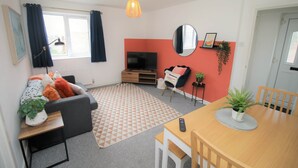 A modern living room with a sofa, a dining table, a TV, and a mirror. - Thesiger 1 (3 beds) (Cardiff)