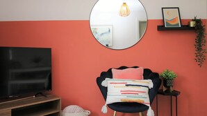 A living room with a television, a round mirror, a chair with a colorful cushion, a hanging light fixture, and a small shelf with a plant. - Thesiger 1 (3 beds) (Cardiff)