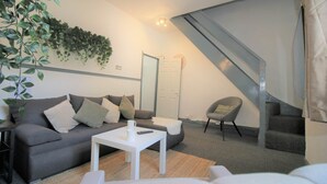 A modern living room with a grey sofa, a white coffee table, and a grey armchair. There is a staircase with a grey railing leading to an upper level. - Fitzroy Street (3 beds) (Cardiff)