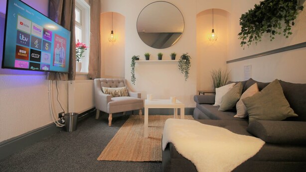 A modern living room with a flat-screen TV, a round mirror, and a fireplace. - Fitzroy Street (3 beds) (Cardiff)