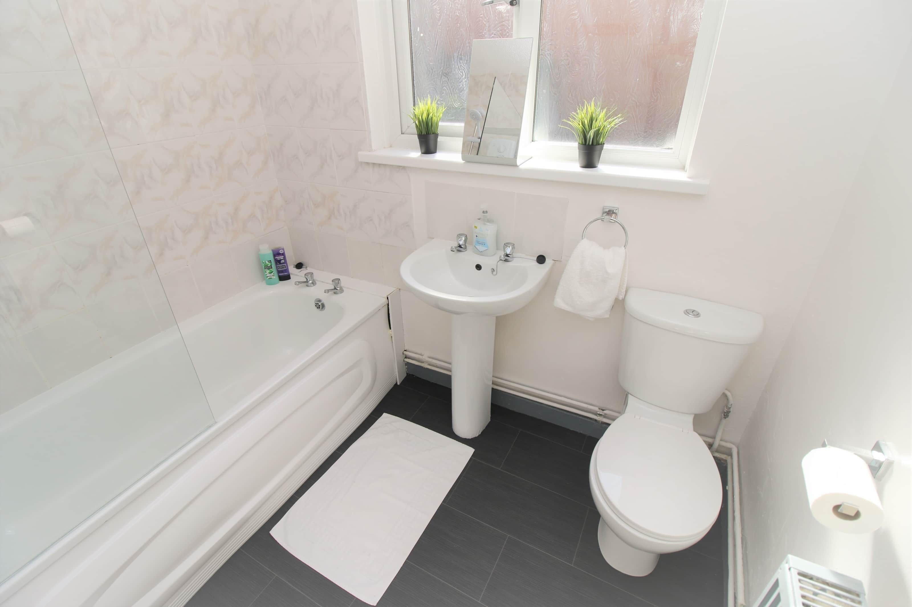 Ein Badezimmer mit Badewanne, Waschbecken und Toilette. Auf der Fensterbank stehen zwei Blumentöpfe.