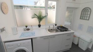 A compact kitchen with a washing machine, a sink, a small potted plant, and a window with a view of buildings. - Fitzroy Street (3 beds) (Cardiff)